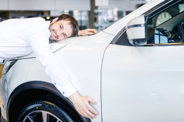 Yakışıklı adam galeride yeni arabasını kucaklıyor.