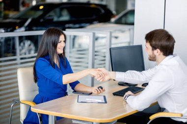 Gülümseyen satıcı araba galerisinde müşteri elini sıkıyor.