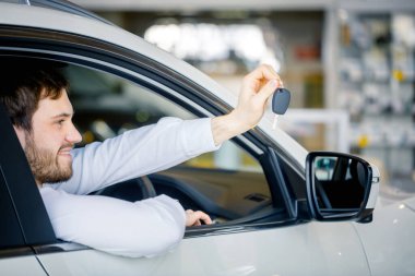 Genç adam arabasında gülümsüyor ve tezahürat yapıyor.