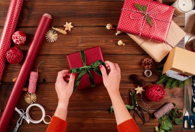 Noel tatili için kırmızı hediye kutularını süsleyen kadın elleri. Eller yukarı..