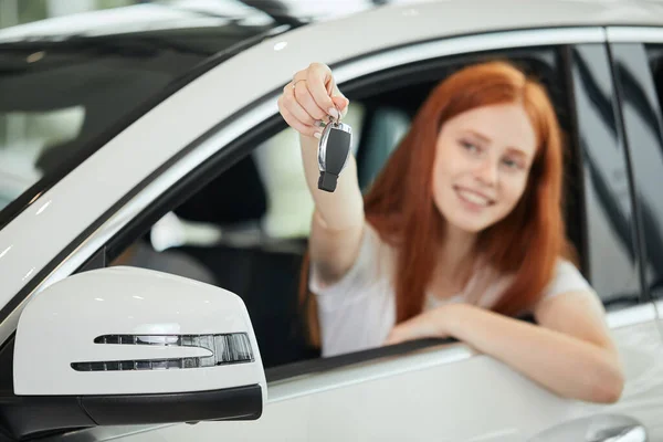 Overjoyed vezető nő mosolyog, és új kulcsot mutat, miközben ül az autó bemutatótermében — Stock Fotó