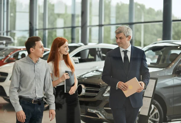 자동차 판매 담당자는 대리점의 고객들에게 차의 기능에 대해 말 합니다. — 스톡 사진