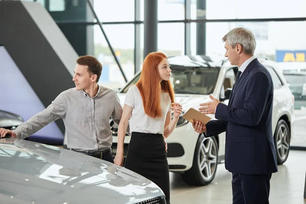 Car sales manager telling about the features of the car to the customers at the dealership