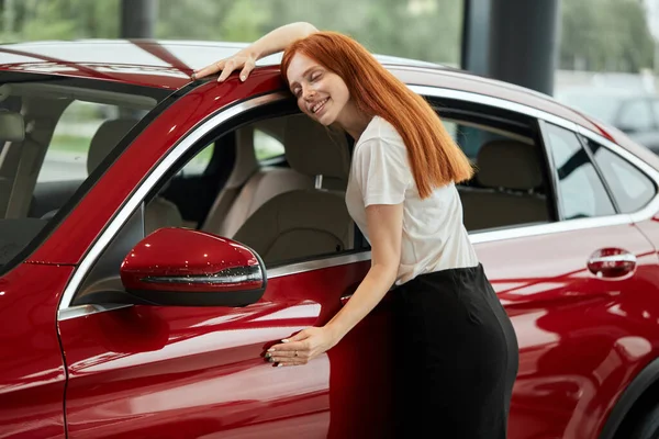 Boldog kaukázusi nő átöleli az új autóját az autókereskedésben — Stock Fotó