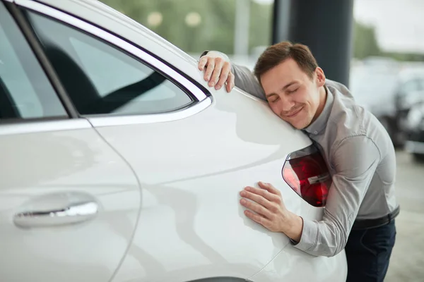 Homem feliz abraçando carro novo, estando completamente satisfeito com a compra . — Fotografia de Stock