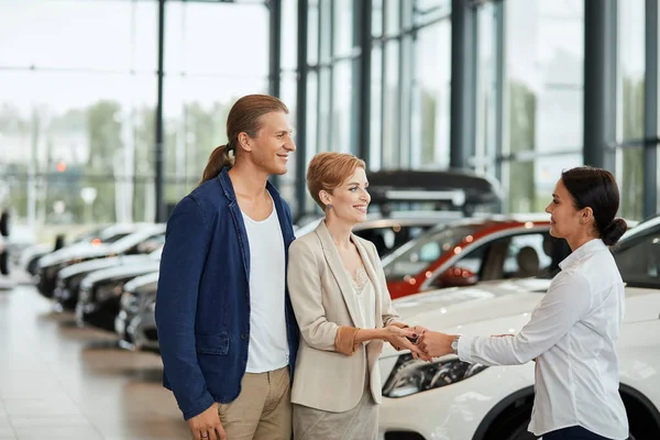 Gerente de ventas de coches que habla de las características del coche a los clientes en el concesionario — Foto de Stock