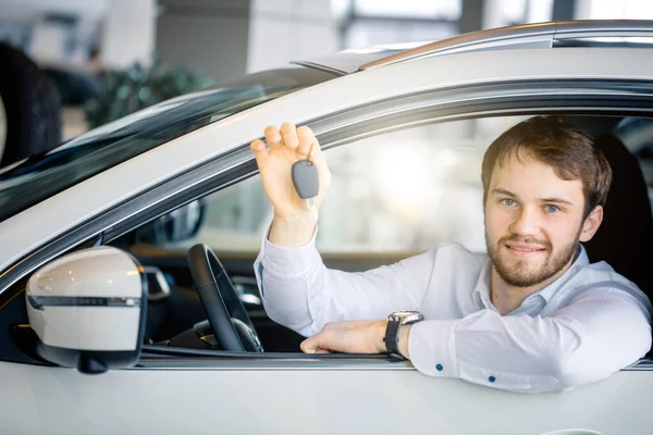 Giovane uomo allegro che mostra la chiave nella sua auto in concessionaria — Foto Stock