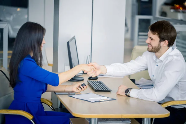 Vendedor sonriente sacudiendo una mano del cliente en la sala de exposición del coche — Foto de Stock