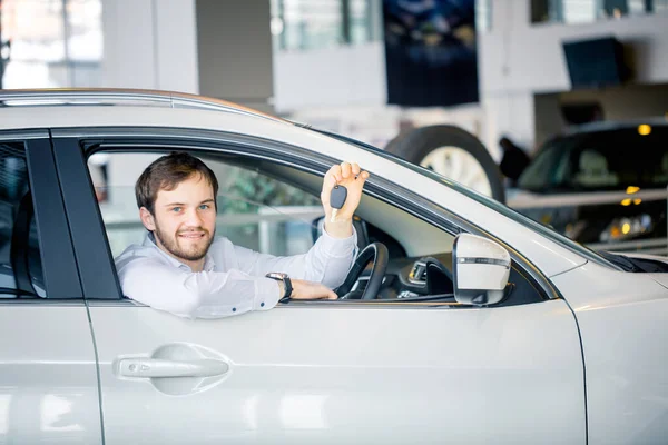 Giovane uomo allegro che mostra la chiave nella sua auto in concessionaria — Foto Stock