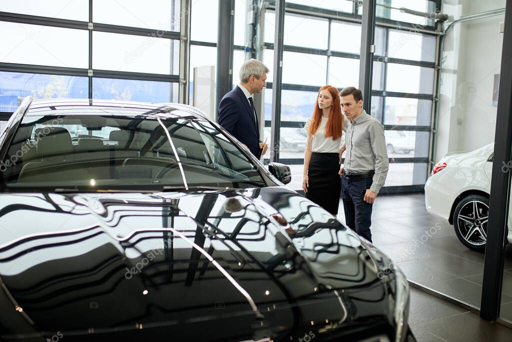 Car sales manager telling about the features of the car to the customers at the dealership