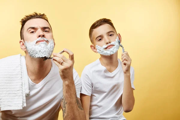 Father and son shaving on yellow background