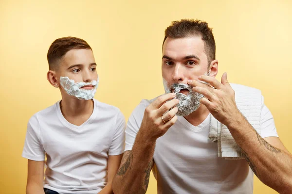 Padre e hijo afeitándose sobre fondo amarillo — Foto de Stock