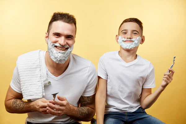 Padre e hijo afeitándose sobre fondo amarillo — Foto de Stock