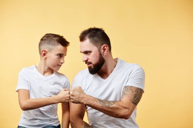 Baba ve oğul ciddi bir şekilde birbirlerine bakıyorlar, yumruklarını bir arada tutuyorlar, dövüşmeye hazırlar.