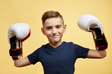 Büyük boks eldivenli küçük çocuk yarışmayı kazanıyor, sarı arka plan stüdyosu