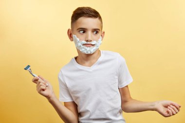 Şok edici çocuk sarı arka planda tıraş olmaya hazırlanıyor.