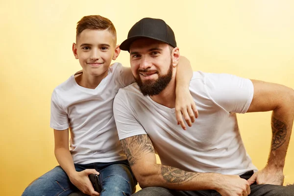 Pai barbudo e pequeno filho sorriso para câmera no fundo amarelo — Fotografia de Stock