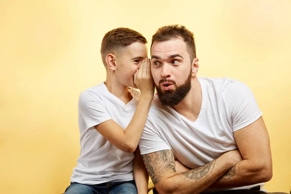 Niño dice secreto para su padre aislado enfondo amarillo —  Fotos de Stock