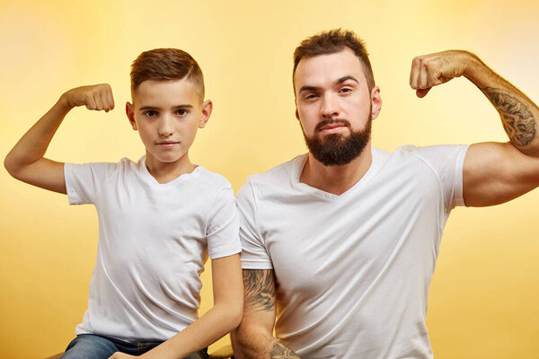 bearded father and his son looking at camera and smiling while show biceps
