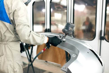 Özel garajda araba parçaları boyayan, kostüm ve koruyucu giysiler giyen işçiler.