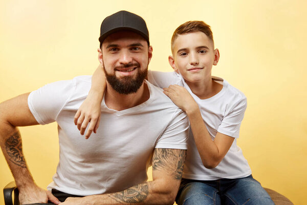 bearded father and little son smile for camera on yellow background