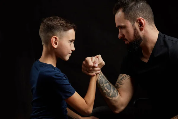 Vader en zoon tijdens vriendschappelijke arm worstelwedstrijd op zwart — Stockfoto