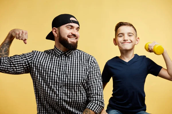 Bebaarde vader en zijn zoon kijken naar de camera en glimlachen terwijl show biceps — Stockfoto