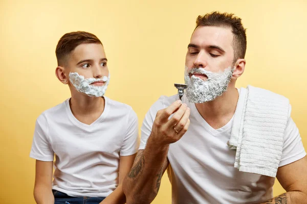 Father and son shaving on yellow background — Stock Photo, Image