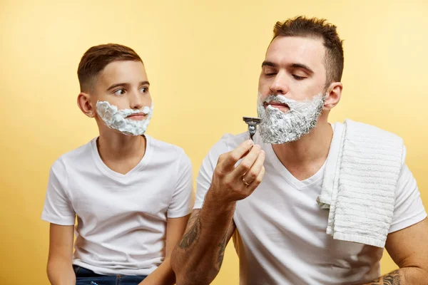 Padre e hijo afeitándose sobre fondo amarillo — Foto de Stock