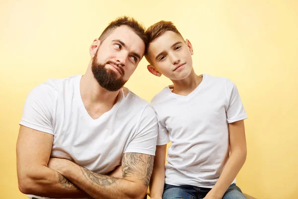 Pai barbudo e pequeno filho sorriso para câmera no fundo amarelo — Fotografia de Stock