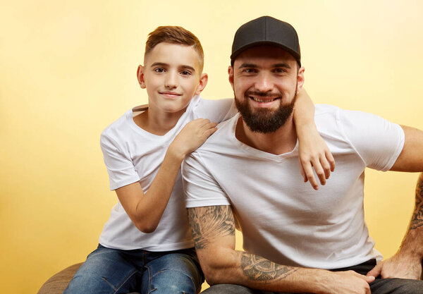 bearded father and little son smile for camera on yellow background