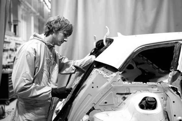 auto repair worker flatten and align metal body car with hammer in garage