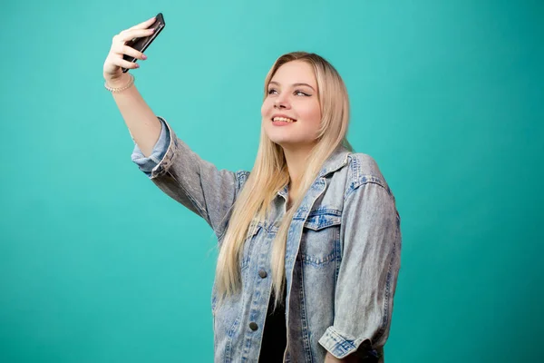 Positivo donna dai capelli biondi prendendo selfie su sfondo blu isolato prendendo in giro con se stessa — Foto Stock