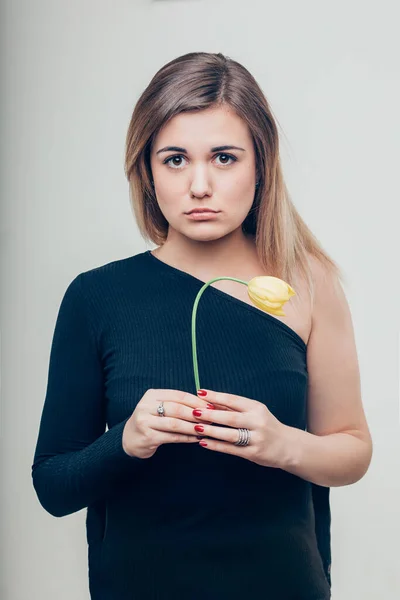Zamknij się Smutna młoda kobieta gospodarstwa martwy kwiat róży podczas patrząc w aparat — Zdjęcie stockowe