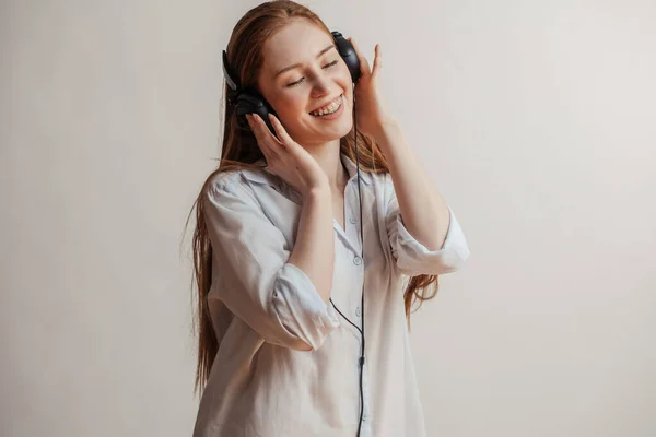 Молодая рыжая женщина расслабляется и слушает музыку с наушниками в помещении — стоковое фото