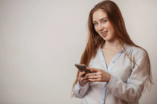 Νεαρή συναισθηματική ελκυστική κοκκινομάλλα γυναίκα κρατώντας smartphone απομονώνονται στο στούντιο — Φωτογραφία Αρχείου