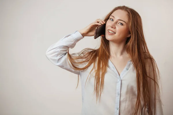 Молодая эмоционально привлекательная рыжая женщина держит смартфон изолированным в студии — стоковое фото