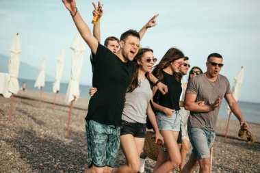 Tatil, tatil. Bir grup arkadaş sahilde eğleniyor, yürüyor, bira içiyor, gülümsüyor ve sarılıyorlar.
