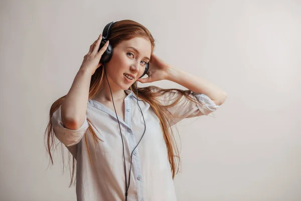 Ung rödhårig kvinna kopplar av och lyssnar på musik med hörlurar inomhus — Stockfoto