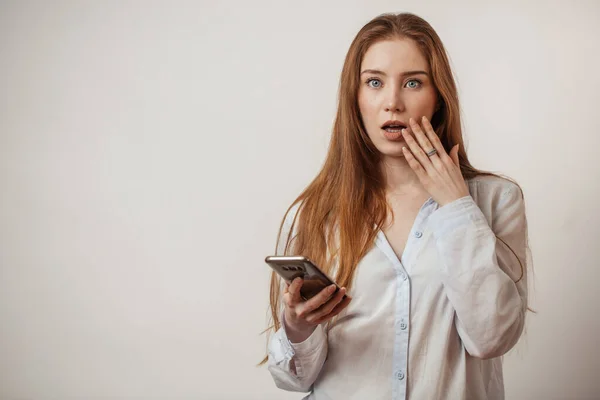 Young emotional attractive redhead female holding smartphone isolated at studio — Stock Photo, Image