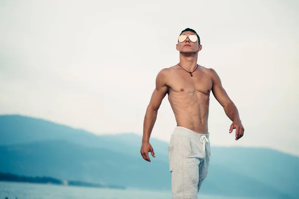 Homem de corpo masculino em óculos de sol na praia com mountauns no fundo — Fotografia de Stock