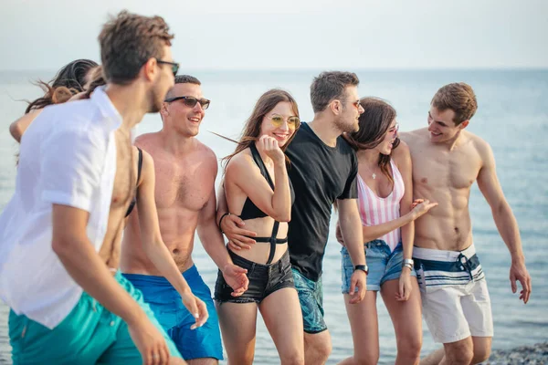 해변에서 친구들과 산책하고, 즐거운 시간을 보내고, 남자들 위에서 피기백을 하고, 즐거운 휴가를 보내는 여자들 — 스톡 사진