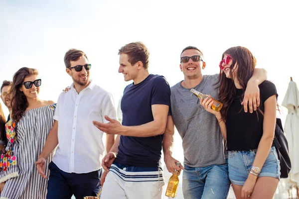 Vacanze, vacanze. gruppo di amici che si divertono sulla spiaggia, camminano, bevono birra, sorridono e si abbracciano — Foto Stock