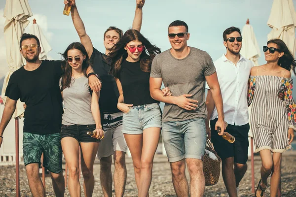 Vacanze, vacanze. gruppo di amici che si divertono sulla spiaggia, camminano, bevono birra, sorridono e si abbracciano — Foto Stock