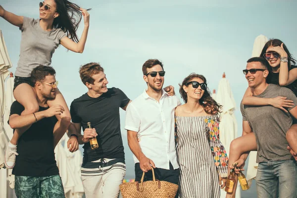Gruppo di amici che camminano in spiaggia, divertirsi, cavalcare le donne su uomini, vacanza divertente — Foto Stock