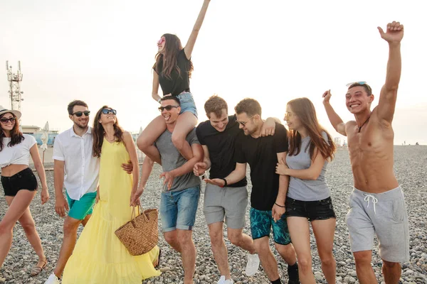 Grupo de amigos caminando en la playa, divertirse, las mujeres a cuestas en los hombres, vacaciones divertidas — Foto de Stock