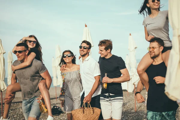 Gruppo di amici che camminano in spiaggia, divertirsi, cavalcare le donne su uomini, vacanza divertente — Foto Stock