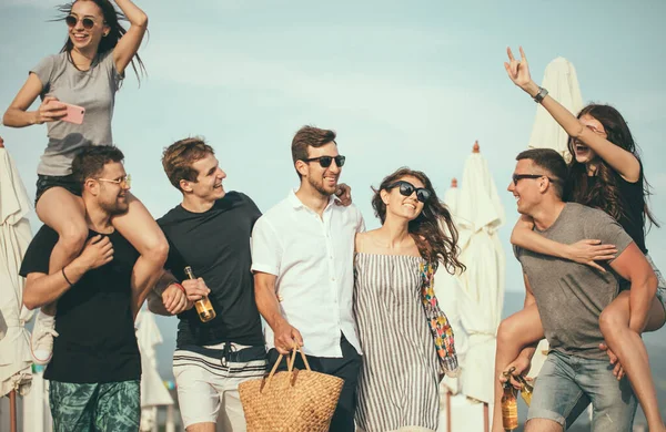 Gruppo di amici che camminano in spiaggia, divertirsi, cavalcare le donne su uomini, vacanza divertente — Foto Stock