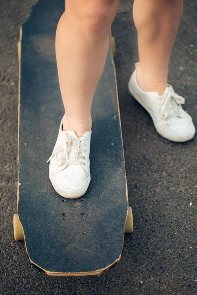 Longboarden en people concept - vrouwelijke benen rijden op longboard langs de weg — Stockfoto