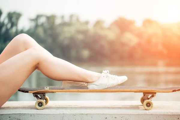 Close-up van trendy vrouwelijke benen ontspannen op een longboard. Ripped jeans mode — Stockfoto